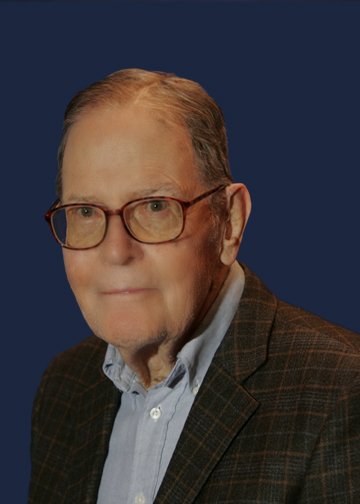 a man with glasses and suit looks into the camera with a subtle smile